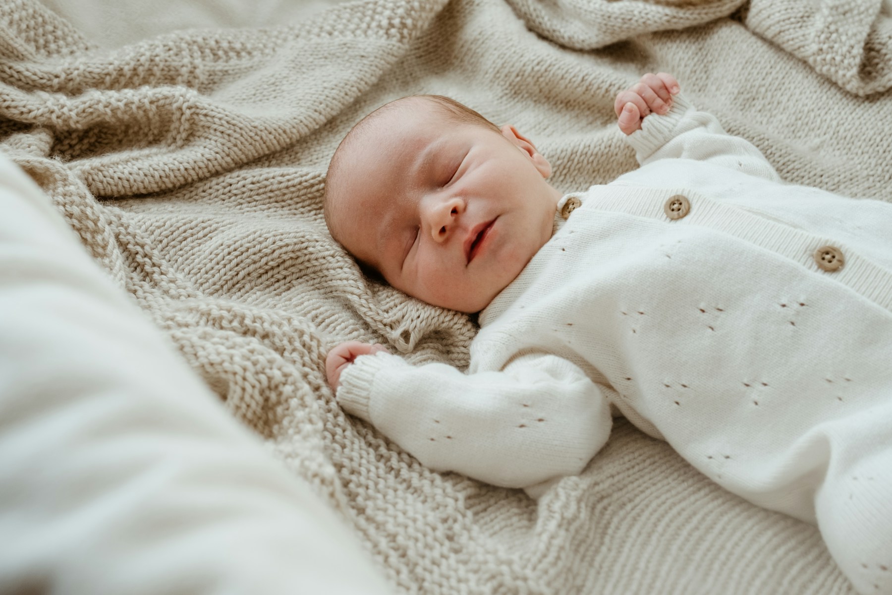 Newborn baby sleeping in soft white clothing on a knitted blanket